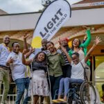 Eine Gruppe junger Menschen mit und ohne Behinderungen posieren für ein Foto und lachen in die Kamera