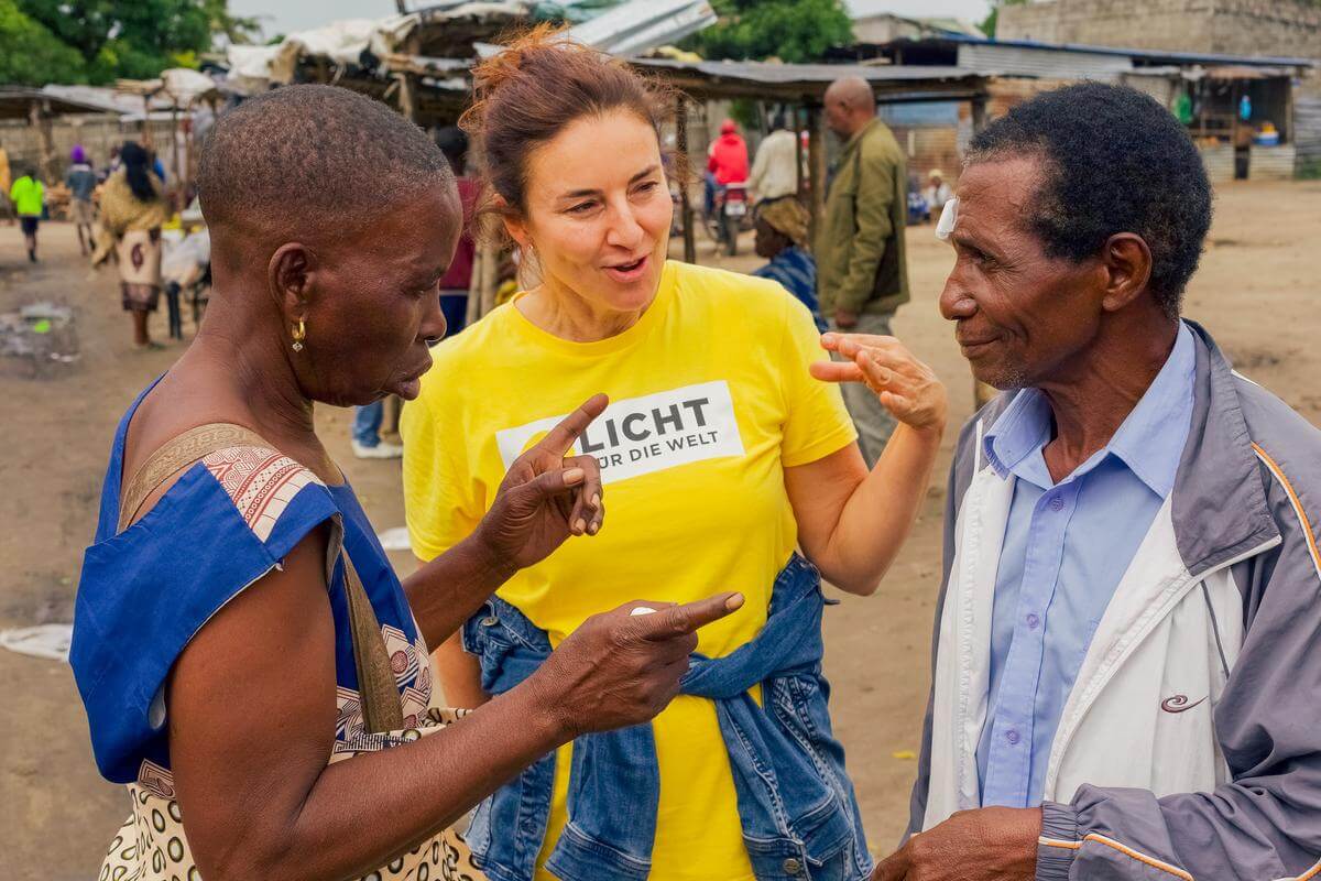 Dr. Irene Ruhswurm im gelben Licht für die Welt T-Shirt spricht mit zwei Erwachsenen in Mosambik