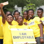 Eine Gruppe von sieben jungen Erwachsenen im gelben Licht für die Welt T-Shirt macht ein Selfie mit dem Schild 
