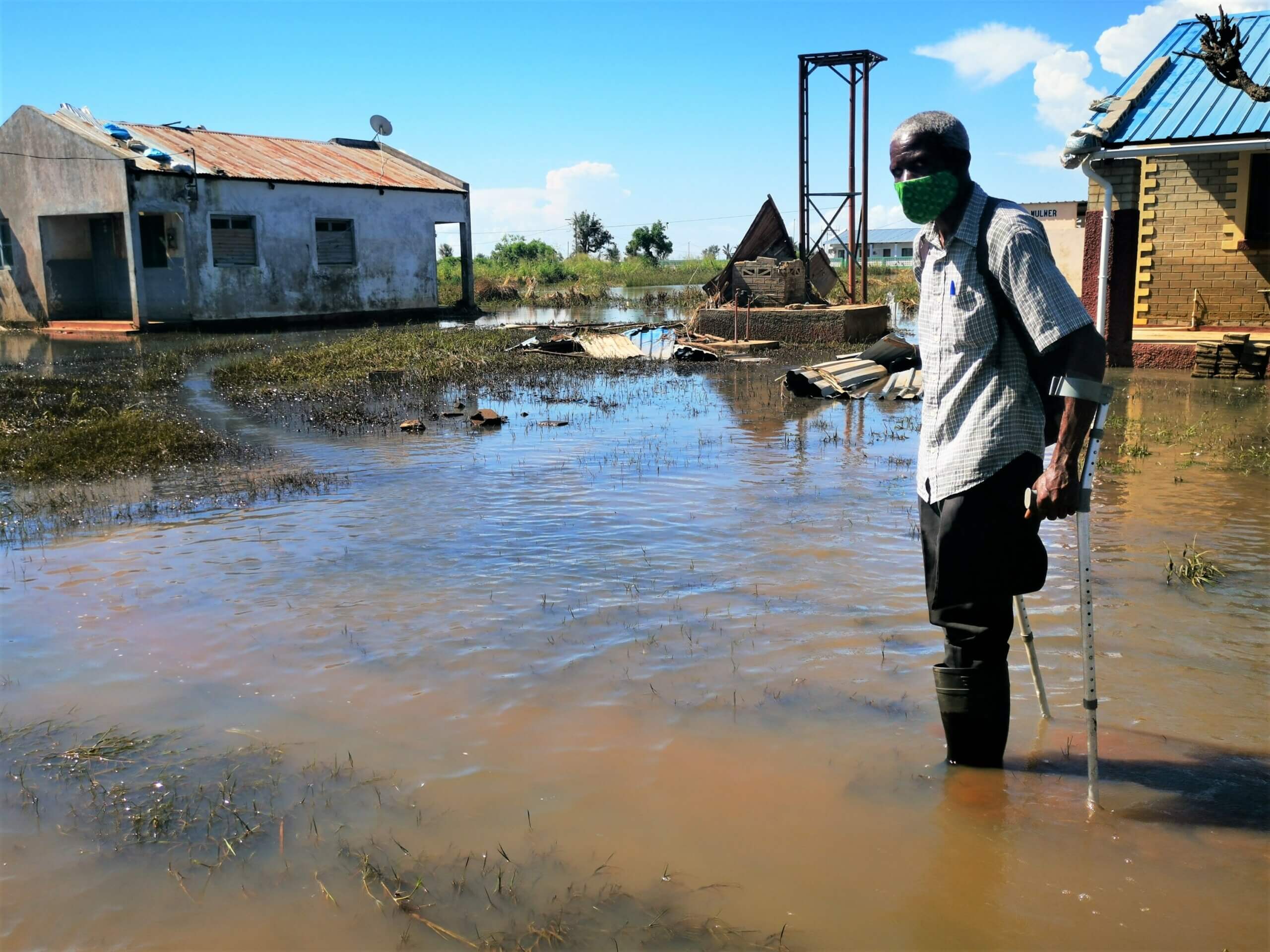 Ein älterer Mann mit Krücken steht vor seinem überfluteten Haus im Südsudan.