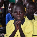 Ein Junge sitzt in der Schule zwischen seinen Klassenkolleg*innen und blickt gespannt nach vorne