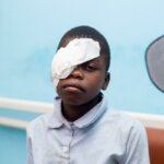 Der Junge Ministro sitzt vor einer blauen Wand im Spital mit einem Augenverband über dem rechten Auge