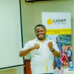 Ambrose Murangira stands smiling in front of a Light for the World sign