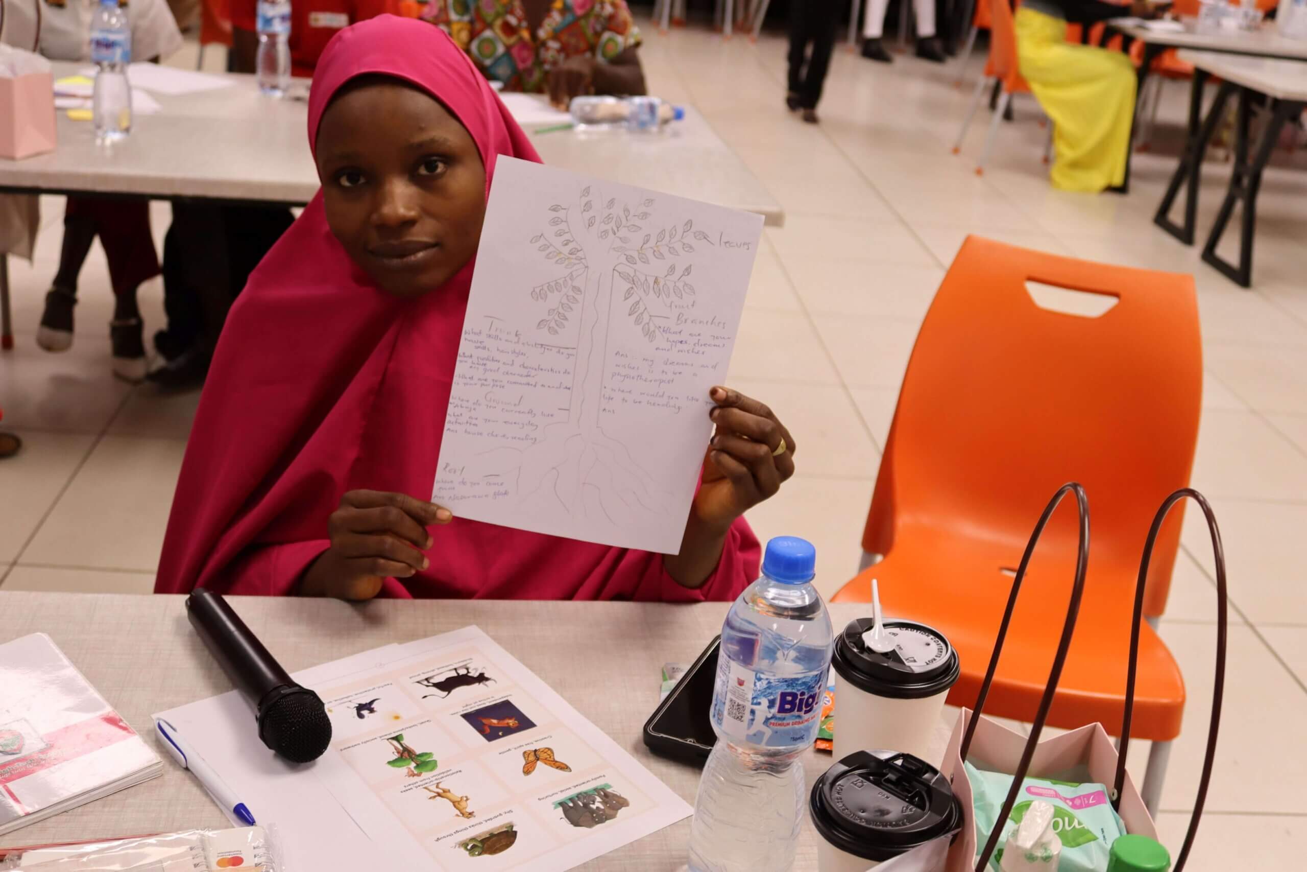 A woman programme participant, wearing red, shows her drawing to the camera after a creative learning session in Nigeria.