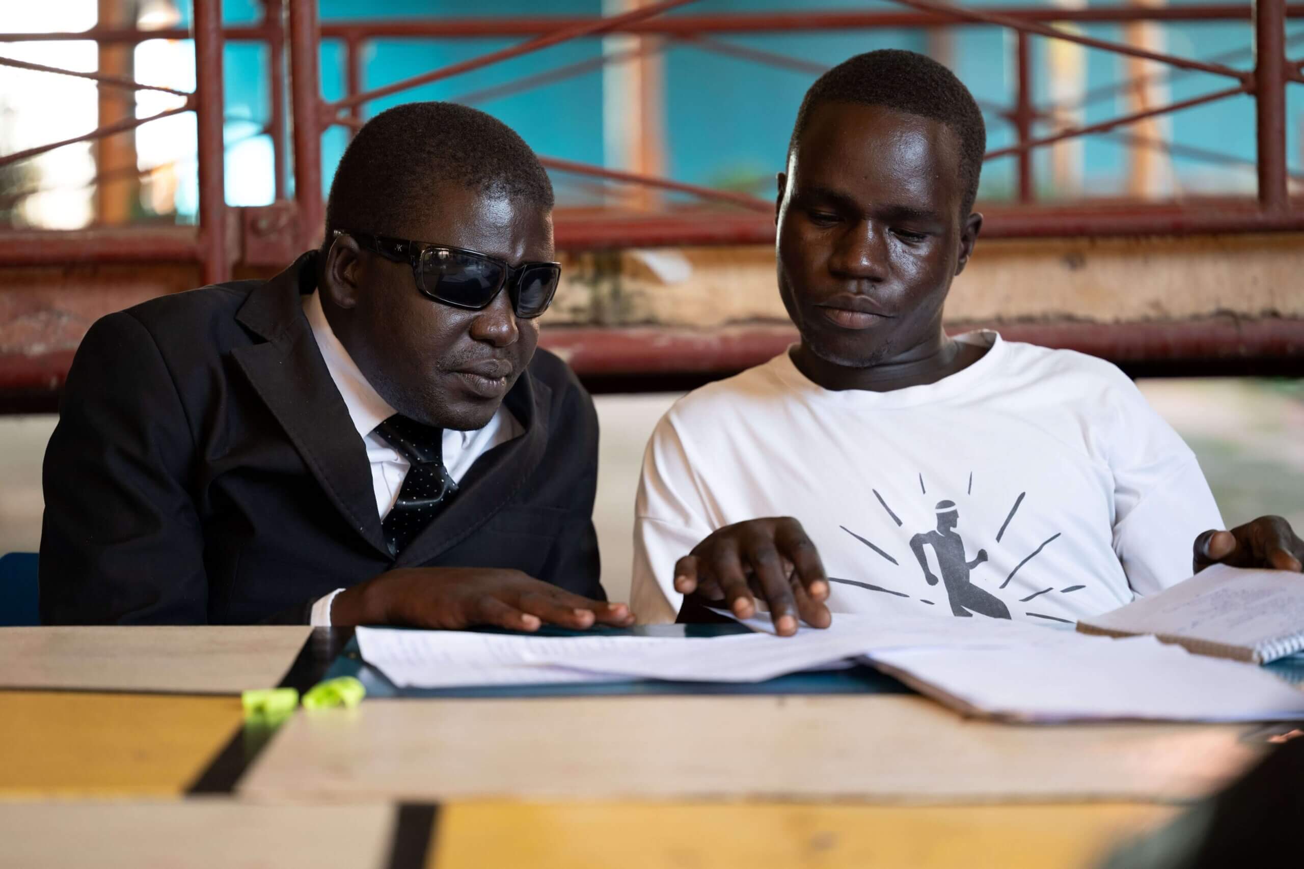 A man with a visual disability, dressed in a black suit, participates with a personal assistant, dressed in a white shirt, during a training session.