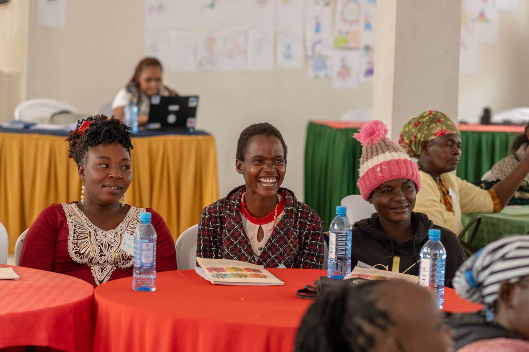 Three women, participants of a core life skills training session, smiling and laughing. They are seated at a table.