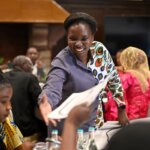 Andera Delfyna, Learning and Innovation Expert at Light for the World, facilitating a co-creation session. She is smiling and handing a piece of paper to a programme participant.