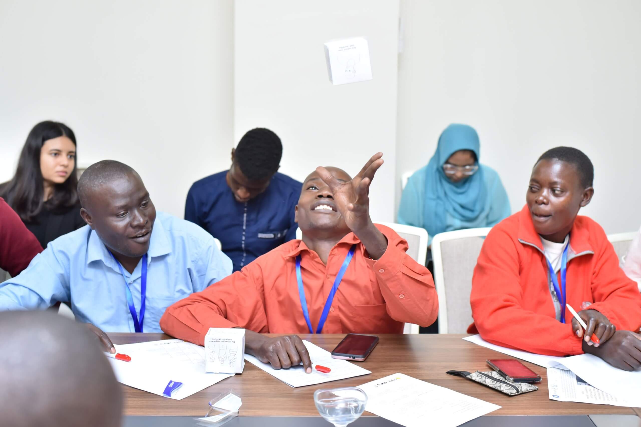 A programme participant engages in a self-discovery game during co-creation week in Nairobi, Kenya. He is seen throwing a piece of paper into the air and looking up at it.