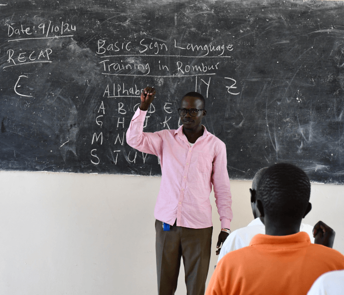 Alex, a student teacher, practises signs in front of a blackboard in a classroom at RNTTI.